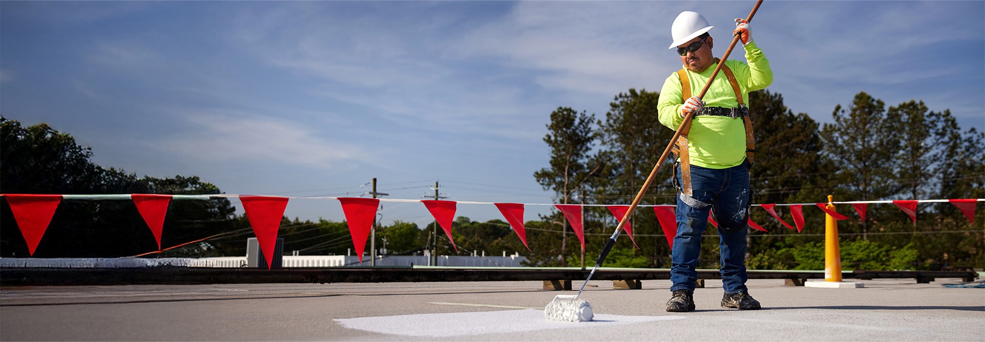 A construction worker using a roller to apply roof coatings to a flat rooftop.