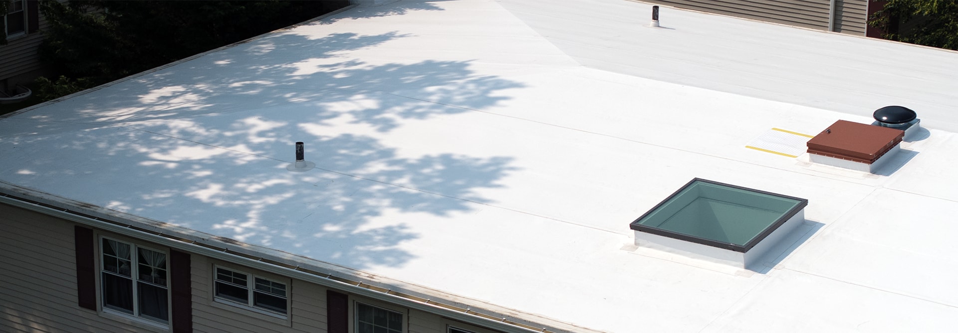 Aerial view of a white commercial roof featuring a glass skylight and rooftop vents.