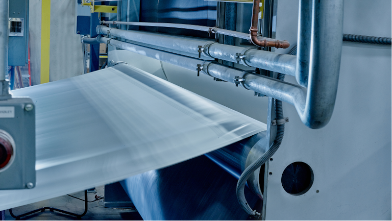 Large-scale industrial machinery manufacturing a continuous white sheet of GAF EverGuard® PVC roofing membrane.