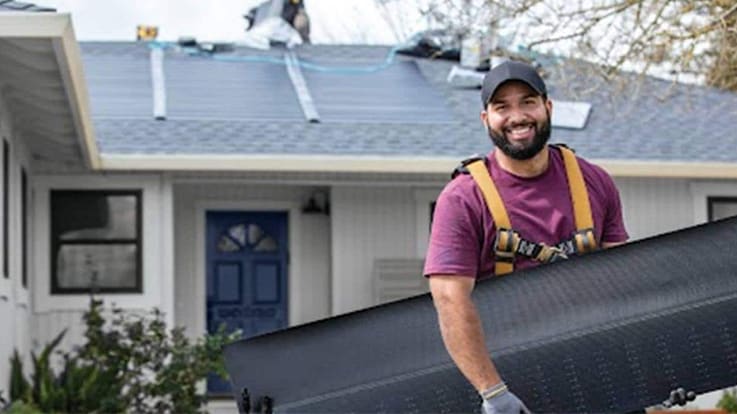 Contratista de techado solar GAF delante de una casa sujetando tejas para techos solares