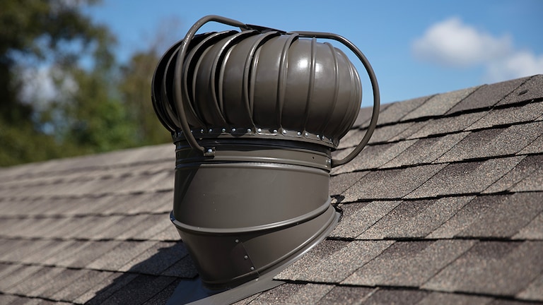 Sideview of a  GAF brand wind turbine that matches the brown asphalt shingles on a sloped roof