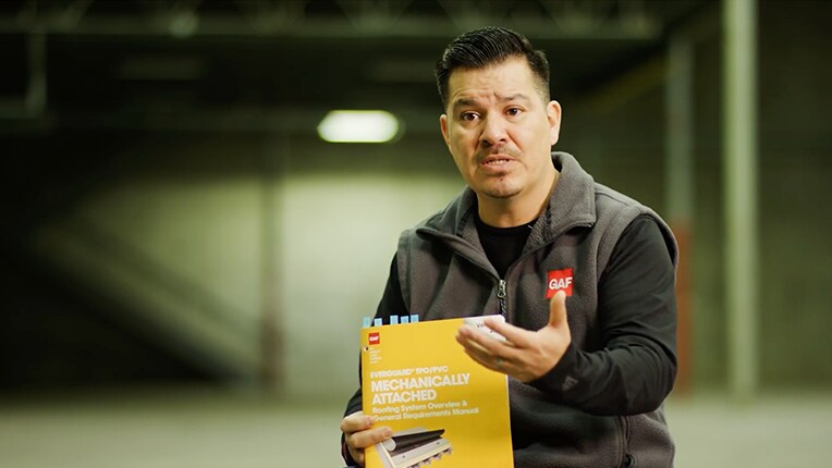 Chino Alvarado sostiene una copia física del Manual de requisitos generales y resumen del sistema de techo con fijación mecánica Everguard TPO/PVC de GAF.
