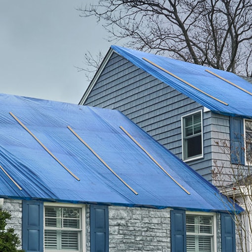 Home with a blue tarp covering roof damage from hurricane